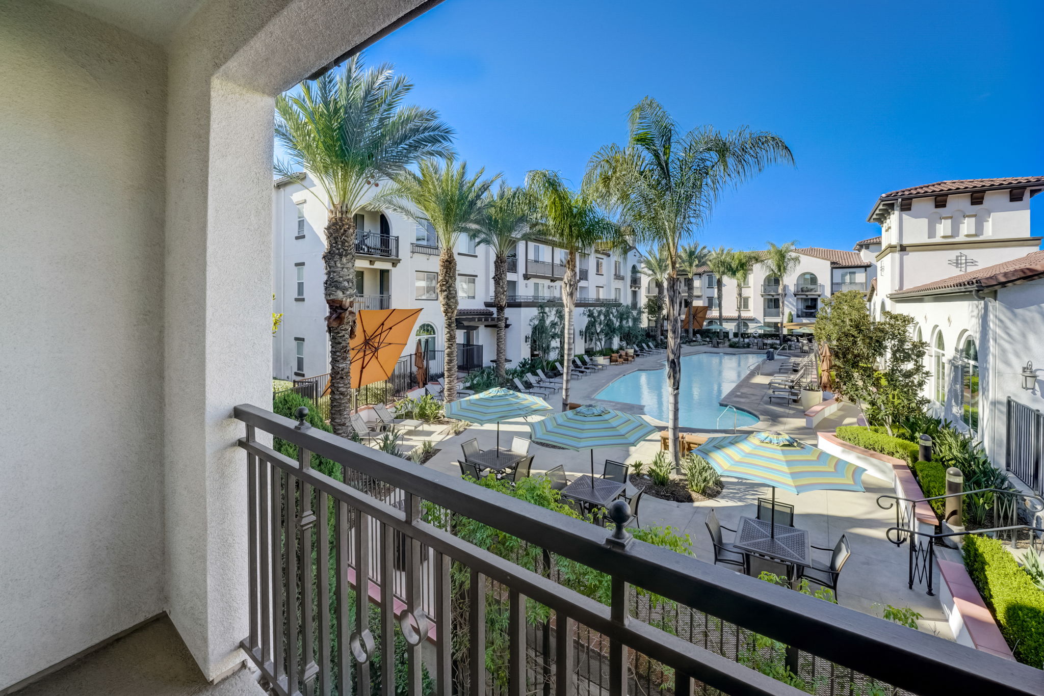 Balcony with view of resort-style swimming pool and buildings at Vistara Apartments in Ontario, CA.